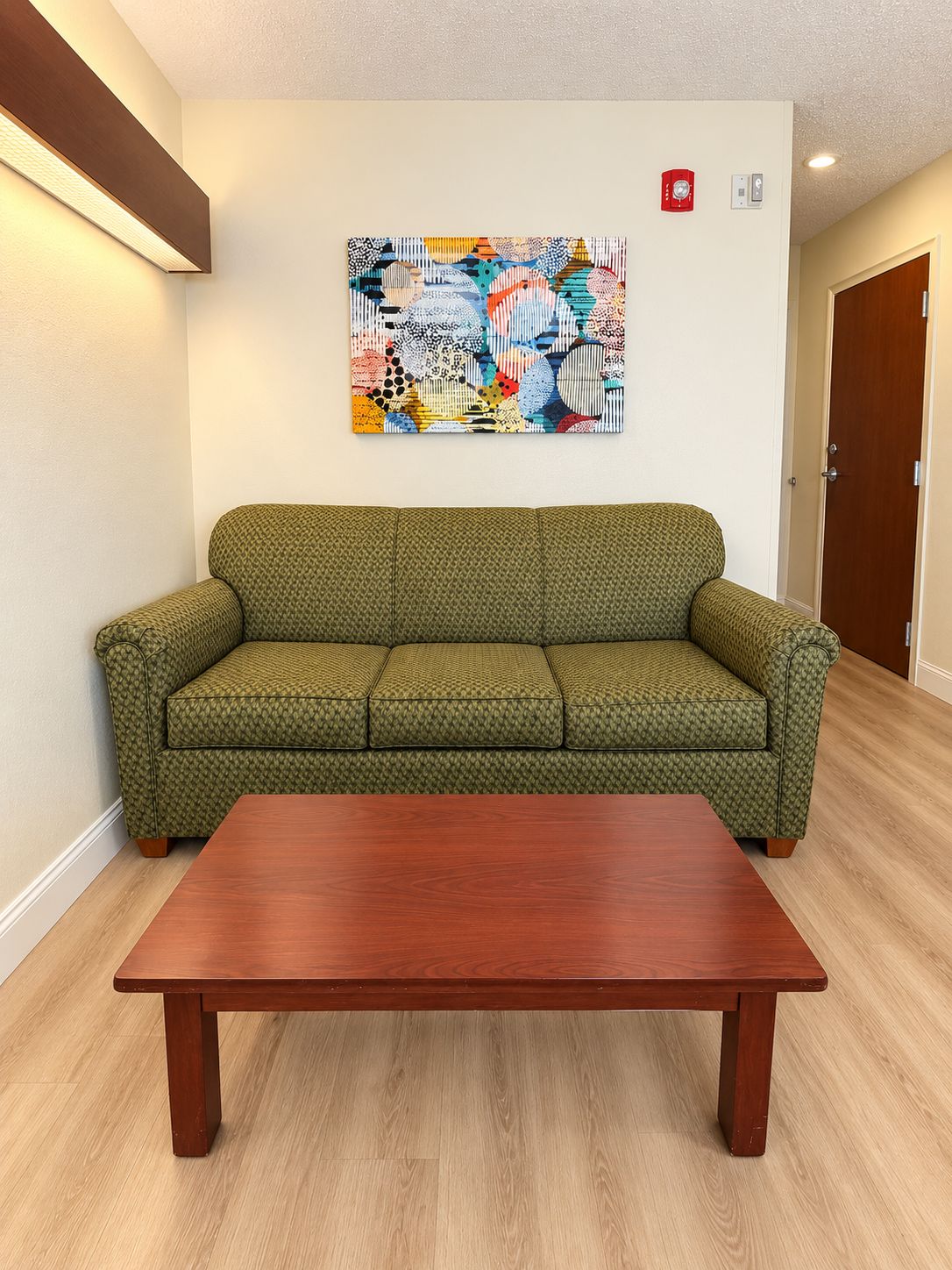 A room with a green patterned sofa, a wooden coffee table, and a colorful abstract painting on the wall.