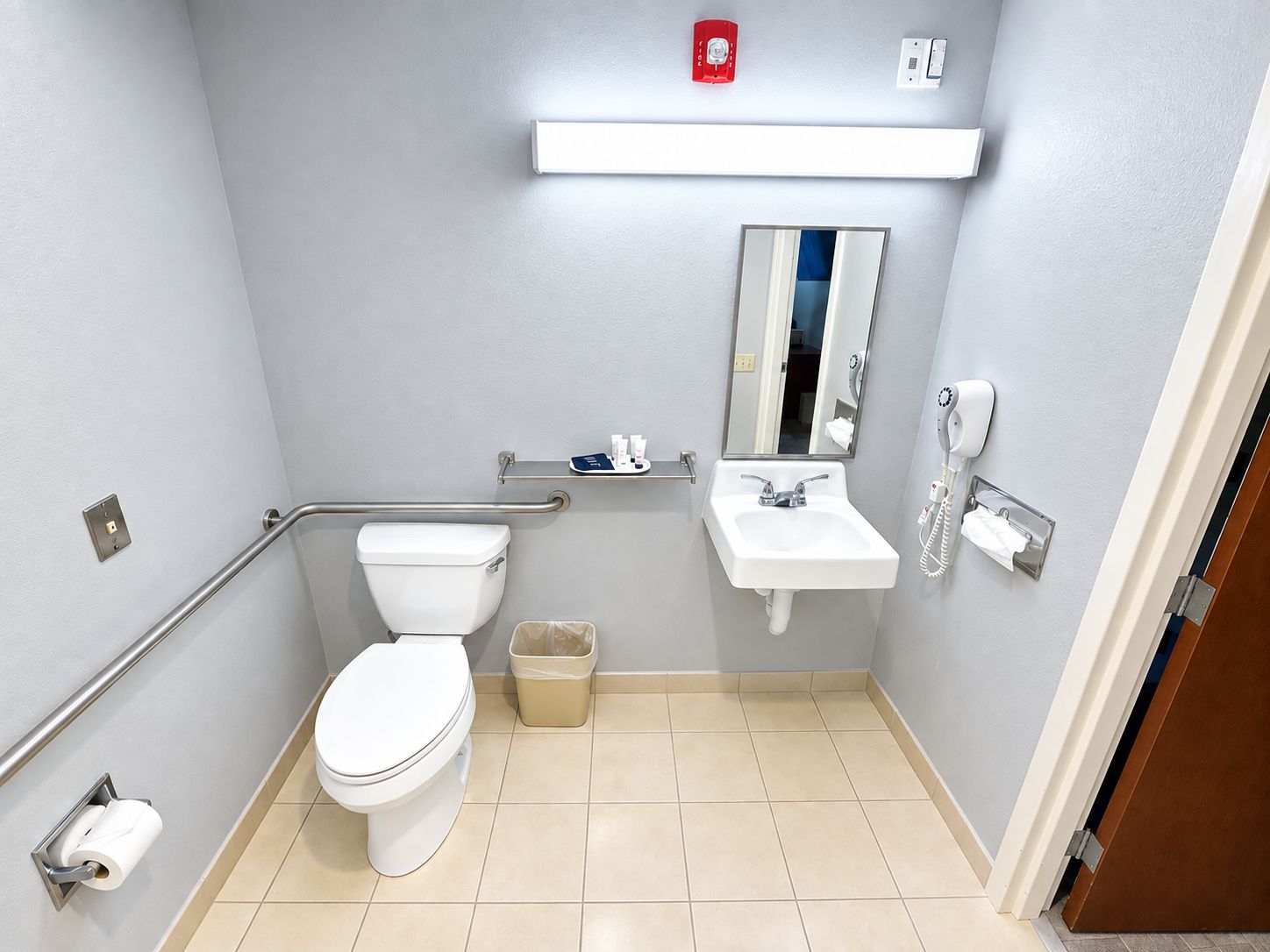 Une salle de bain équipée de toilettes, d’un lavabo, d’un miroir, d’un sèche-mains et d’une poubelle.