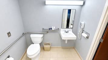 Une salle de bain équipée de toilettes, d’un lavabo, d’un miroir, d’un sèche-mains et d’une poubelle.