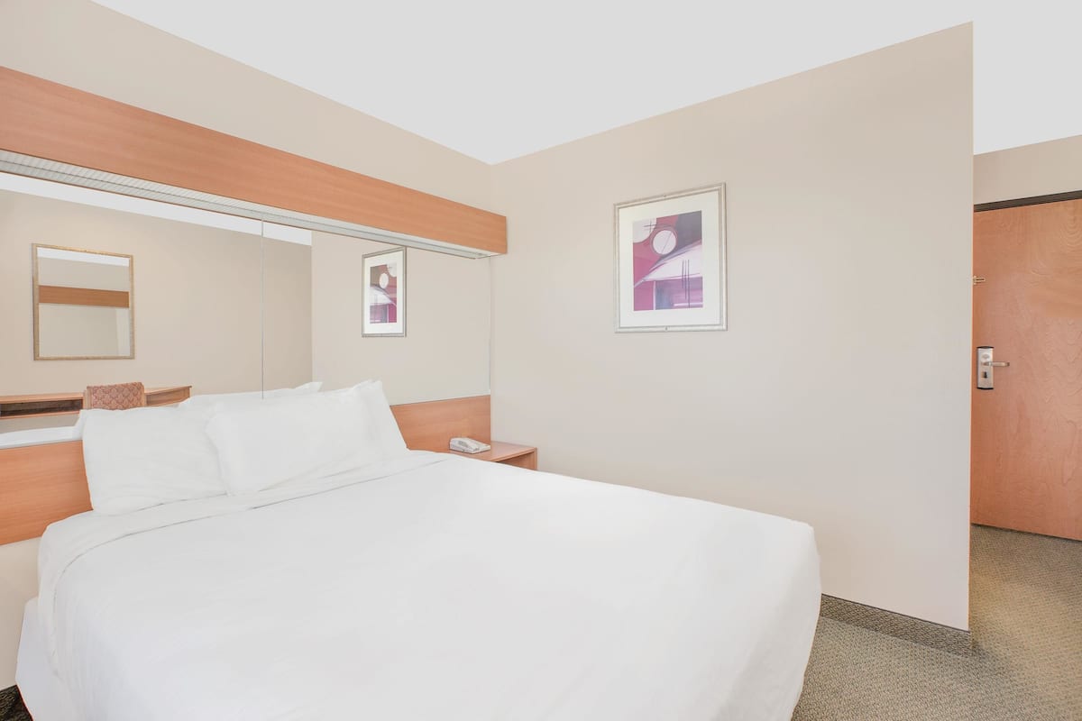 Habitación de hotel con una cama grande, cabecero de madera, mesita de noche con teléfono, espejo y dos cuadros en la pared.