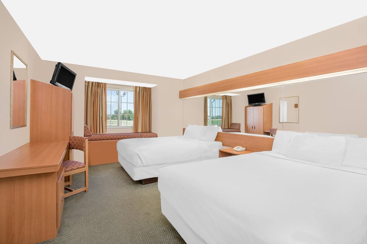 Habitación de hotel con dos camas, un escritorio, una silla, un televisor y una ventana con cortinas.