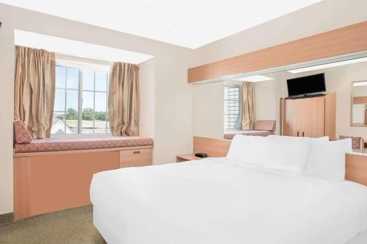 A hotel room with a bed, a desk, a chair, a window with curtains, and a television.