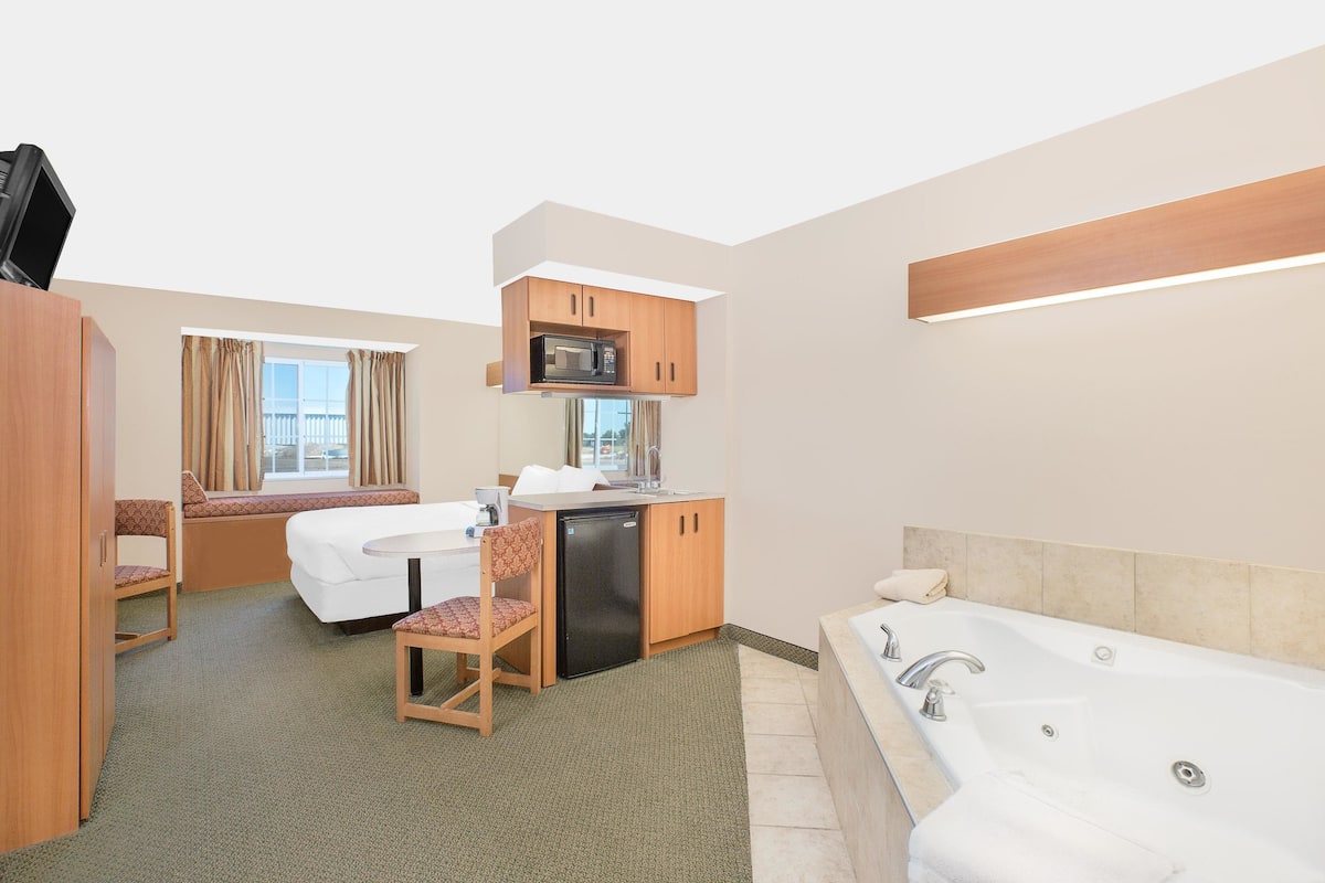 Habitación de hotel compacta con cama, una kitchenette pequeña, zona de estar y baño con bañera.