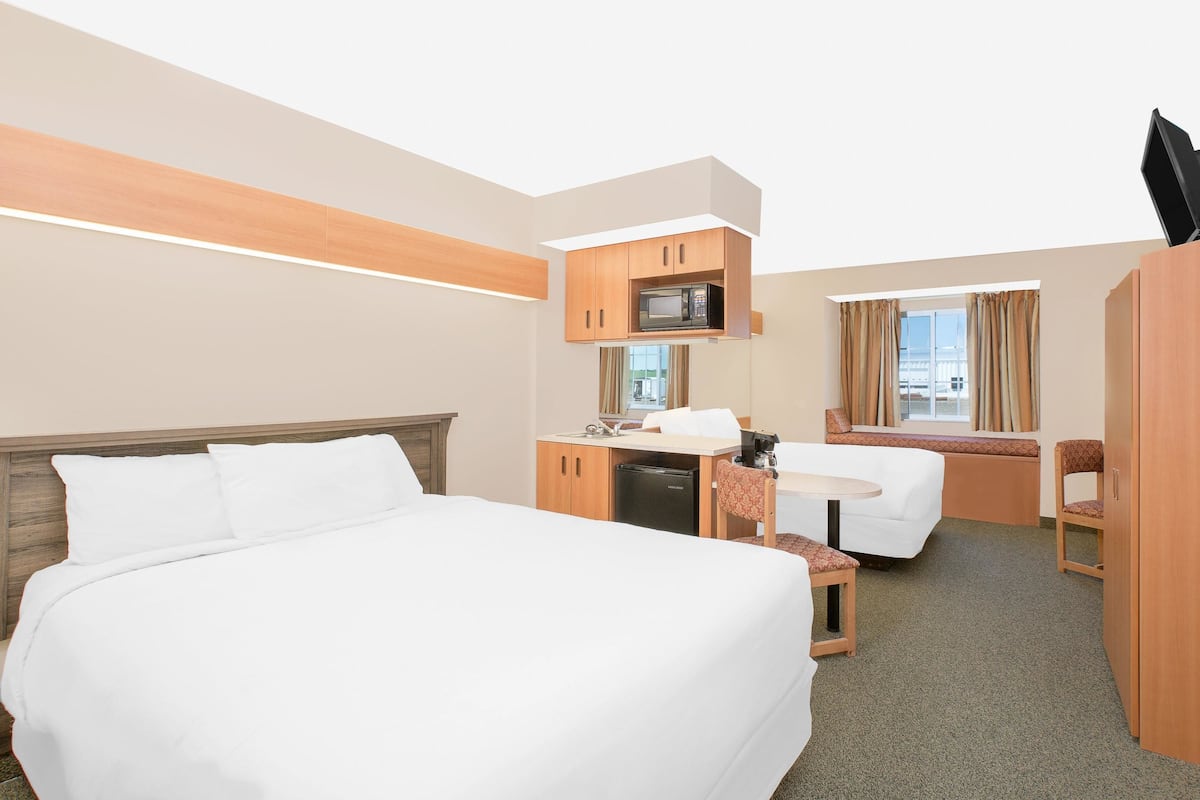 Habitación de hotel con una cama grande, un escritorio con silla, microondas y ventana con cortinas.