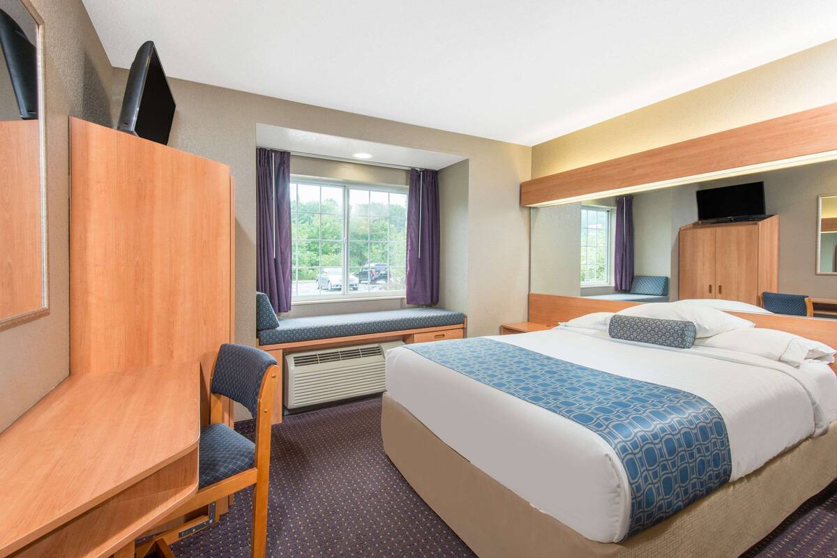 Ein Hotelzimmer mit Bett, Schreibtisch, Stuhl, Fernseher und einem Fenster mit Vorhängen.