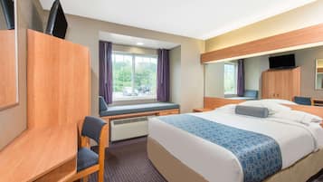Quarto de hotel com cama, escrivaninha, cadeira, televisão e janela com cortinas.