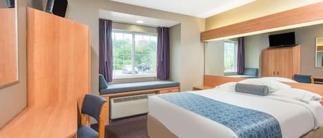Habitación de hotel con cama, escritorio, silla, televisor y ventana con cortinas.
