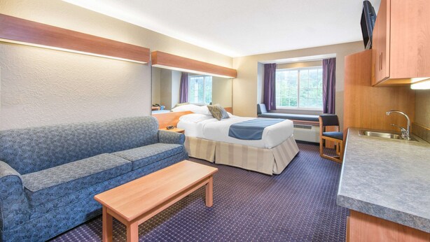 Une chambre d’hôtel compacte comprenant un lit, un canapé, une petite table, un coin cuisine et une fenêtre avec des rideaux.