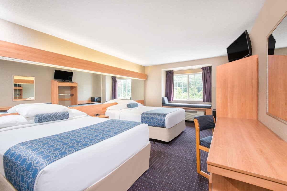 Ein Hotelzimmer mit zwei Betten, einem Schreibtisch, einem Stuhl, einem Fernseher und einem Fenster mit Vorhängen.