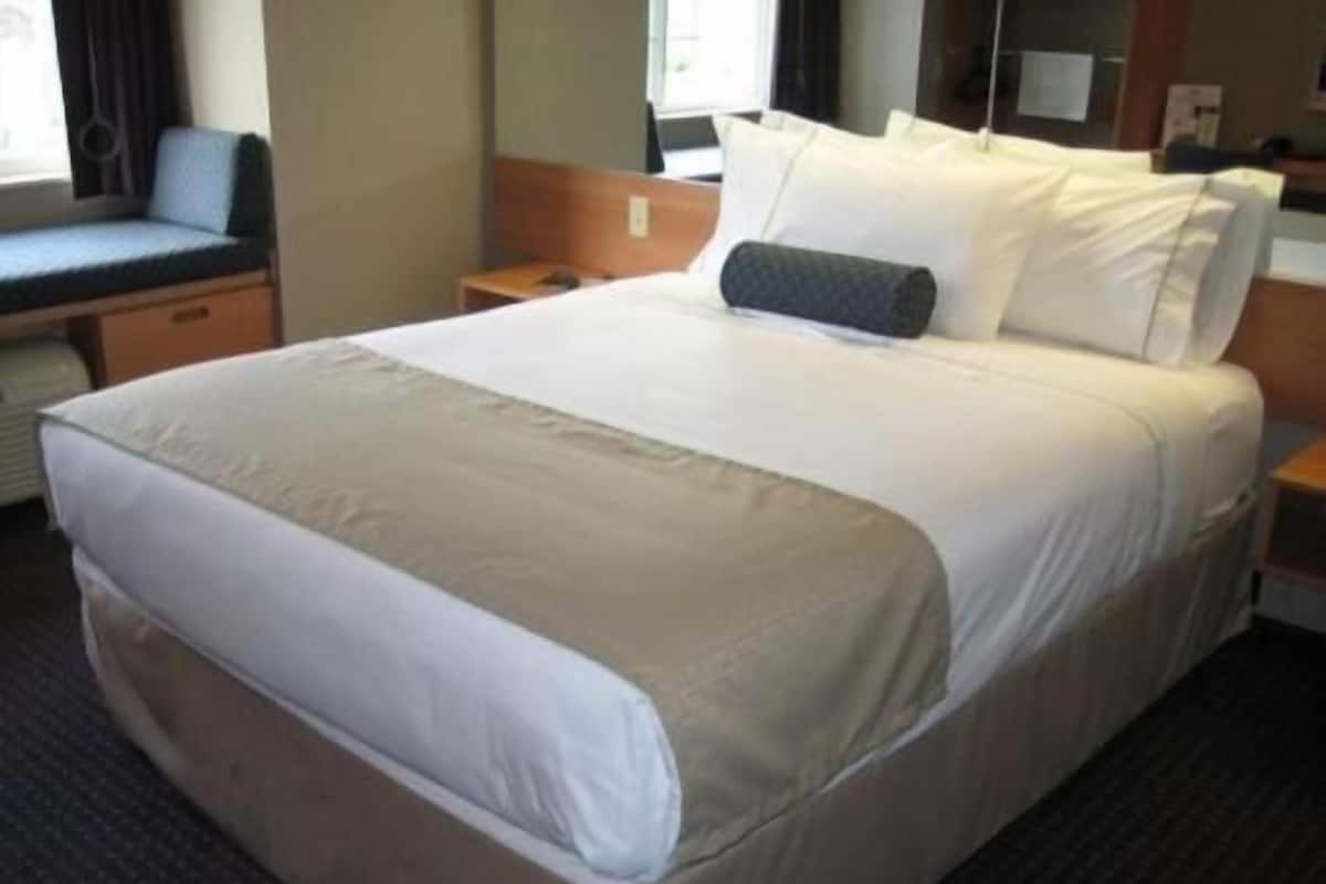 Ein Hotelzimmer mit einem großen Bett, einem Nachttisch, einem kleinen Sitzbereich und einem Fenster mit Vorhängen.