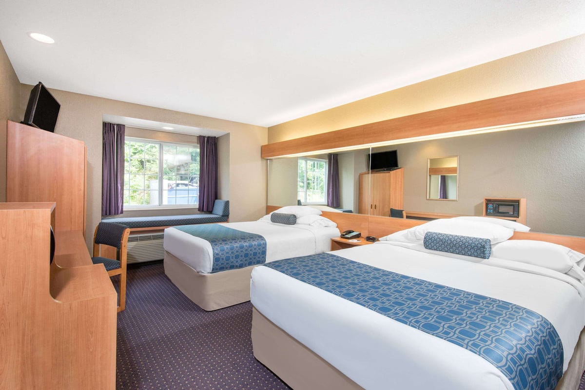 Ein Hotelzimmer mit zwei Betten, einem Schreibtisch, einem Stuhl, einem Fernseher und einem Spiegel.