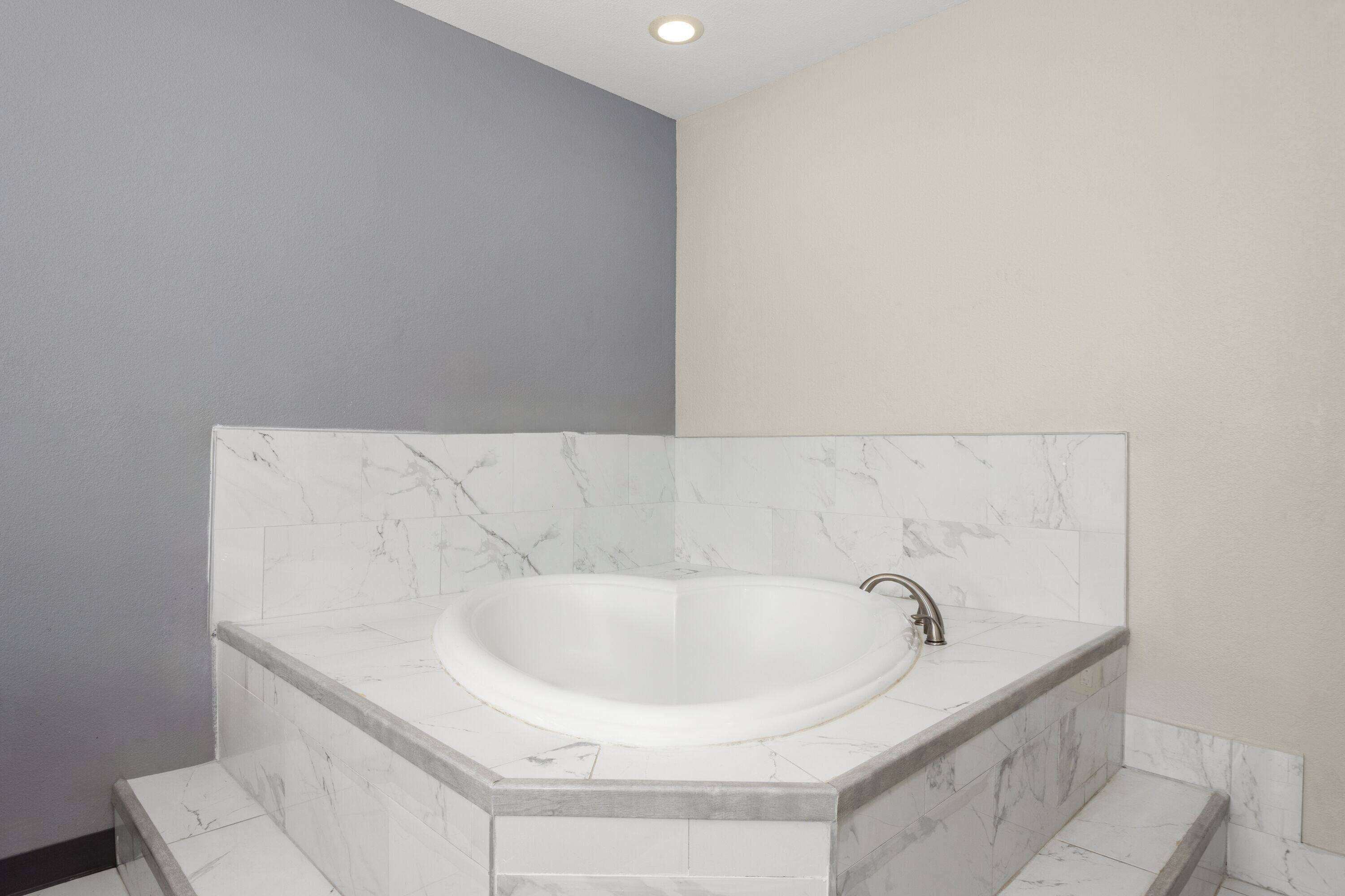 Un baño en esquina con bañera independiente, azulejos de mármol y una paleta de colores neutros.