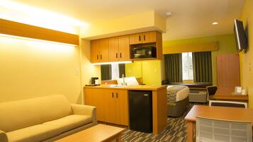 Quarto de hotel compacto com cozinha compacta, sofá, mesa de jantar e TV de tela plana na parede.