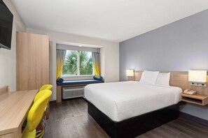 Una habitación de hotel con cama, escritorio, silla, ventana con cortinas y televisor montado en la pared.