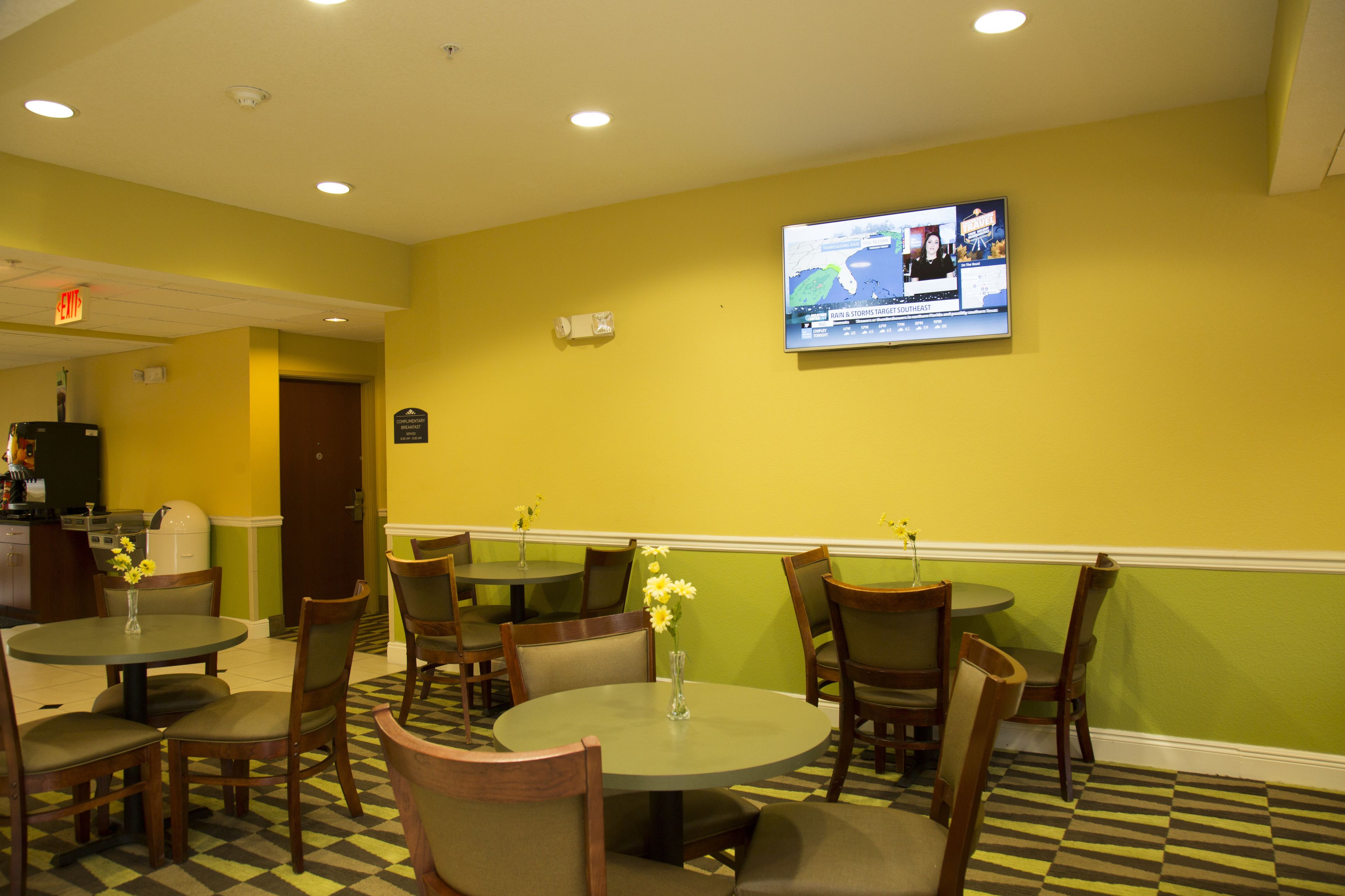 A restaurant with round tables and chairs, a television mounted on the wall, and a checkered floor pattern.