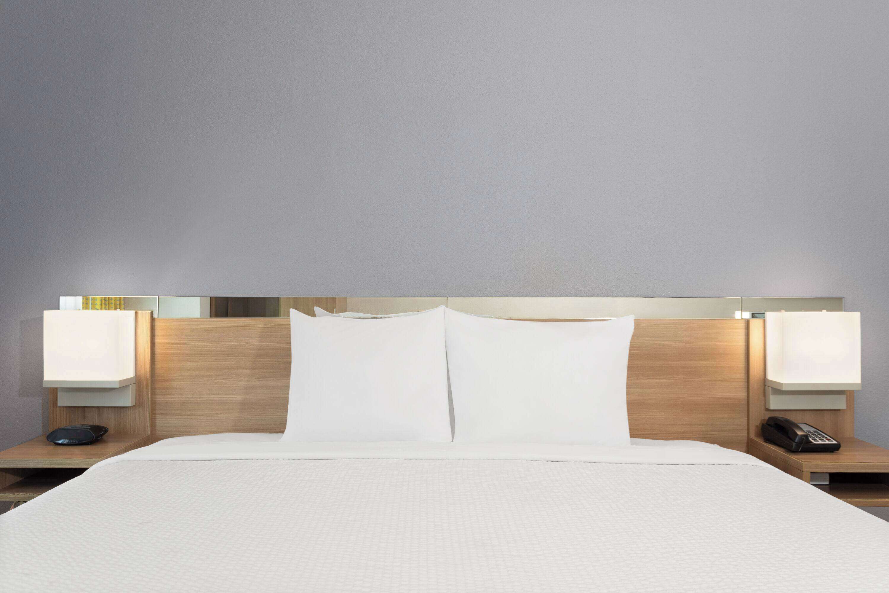A hotel room with a large bed, two bedside tables, a nightstand, and a wall-mounted lamp.