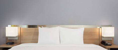 A hotel room with a large bed, two bedside tables, a nightstand, and a wall-mounted lamp.