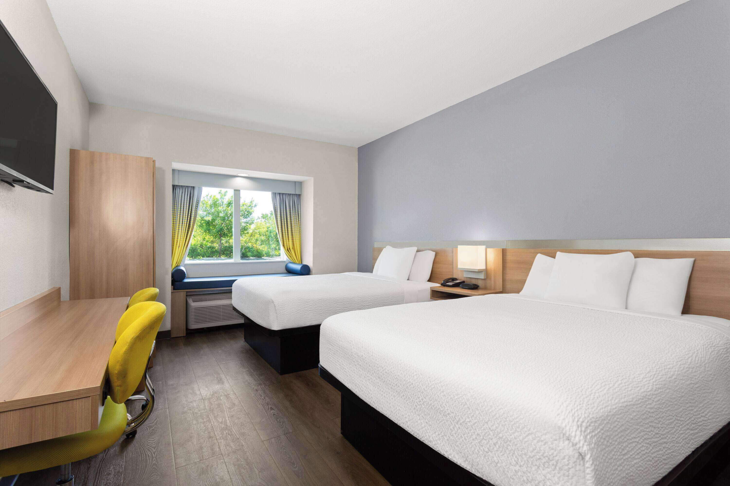 Habitación de hotel con dos camas, un escritorio, una silla, un televisor y una ventana con cortinas.