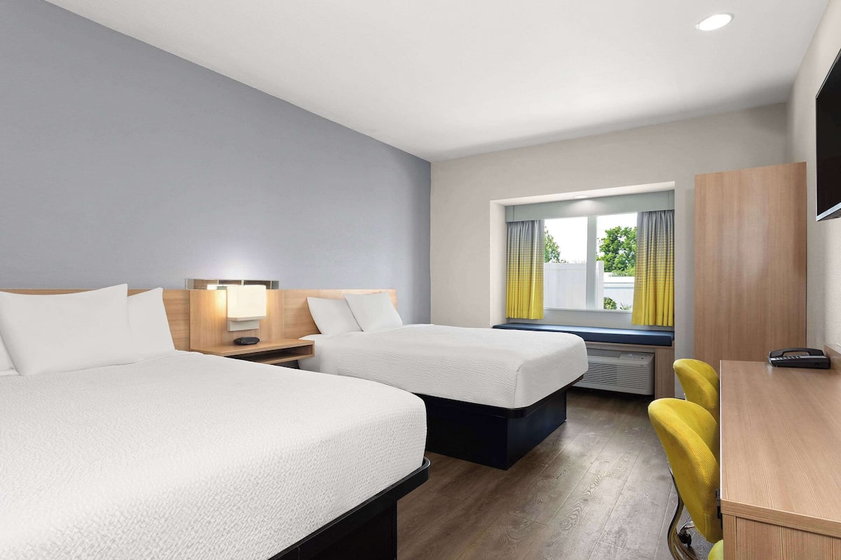 Habitación de hotel con dos camas, un escritorio, una silla, un televisor y una ventana con cortinas.
