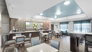 Un comedor moderno con una cocina al fondo, destacando un backsplash de pared de piedra y un amplio ventanal con cortinas.
