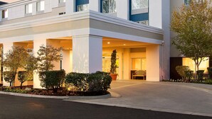Un hotel moderno con un llamativo letrero de 'Sonesta Essential', un acceso cubierto y un jardín frontal ajardinado.