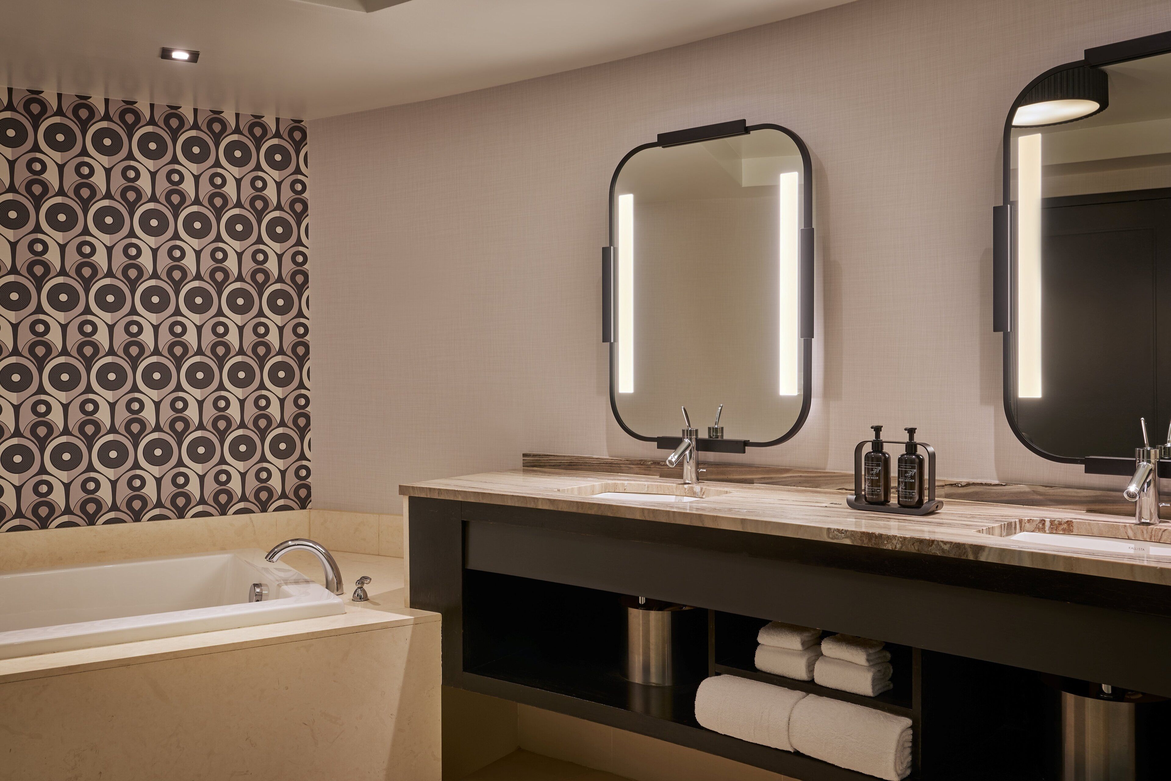A modern bathroom with a large bathtub, two sinks, and a vanity with a mirror.