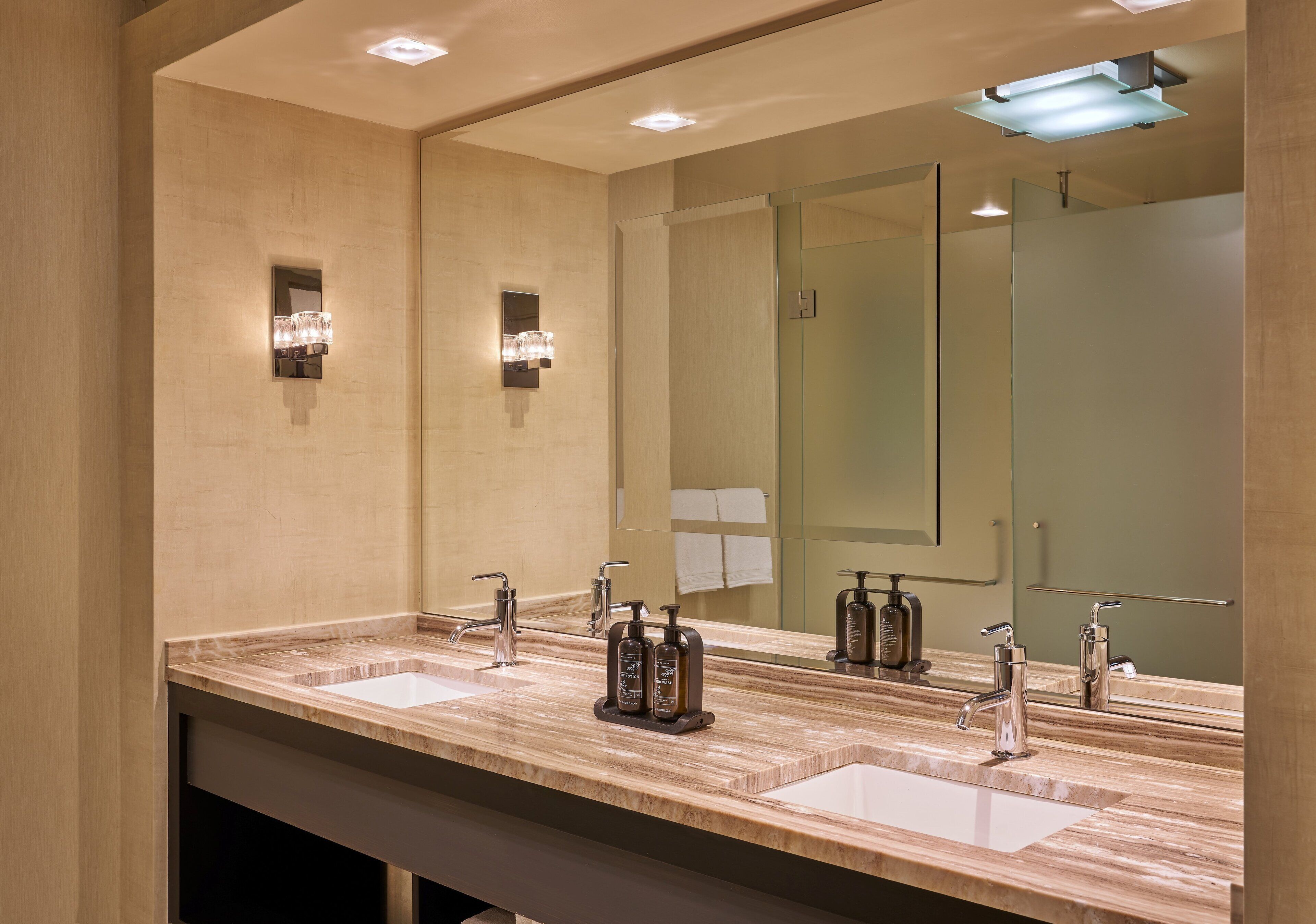 A modern bathroom with two sinks, a large mirror, and wall-mounted lighting.