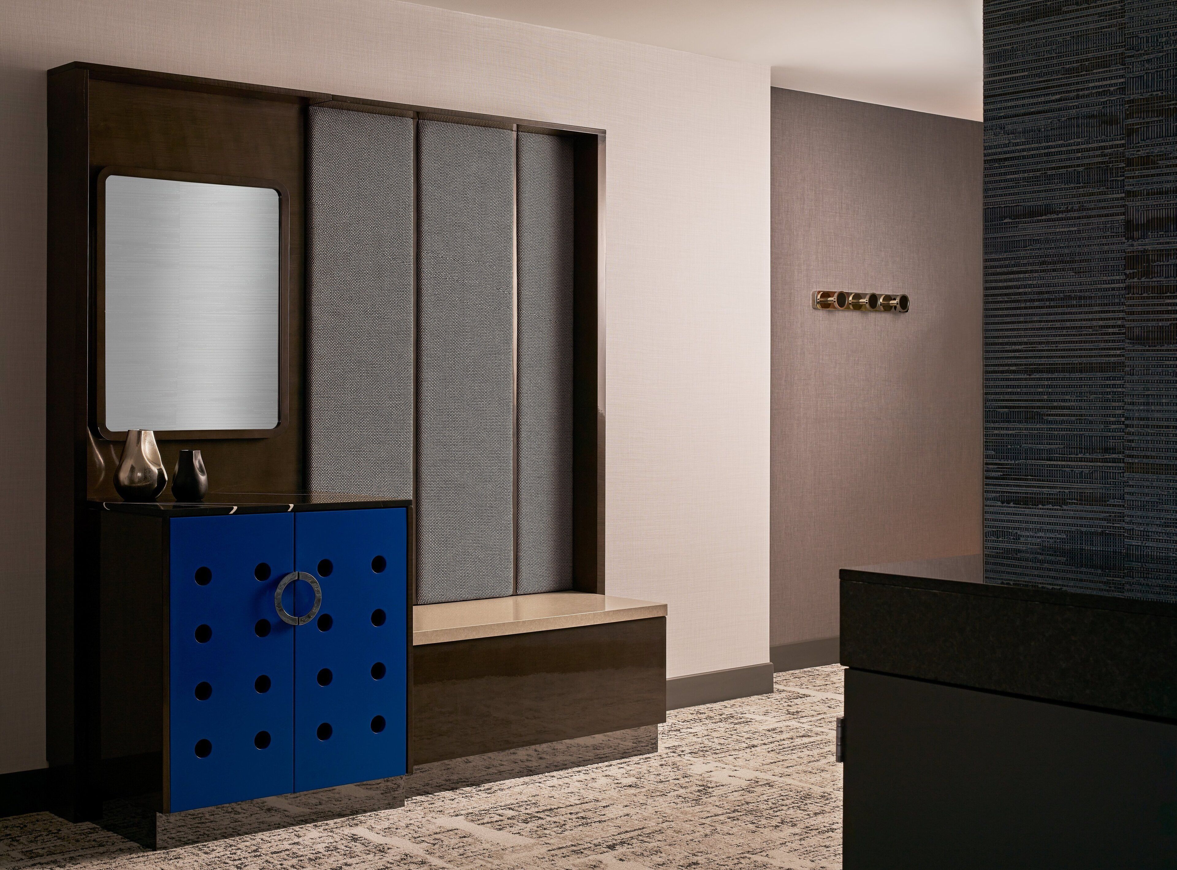 Una habitación de hotel moderna con un ventanal grande, un armario azul y una mesita con una lámpara.