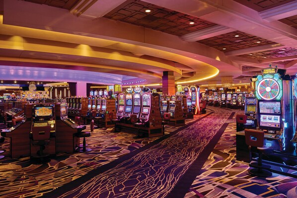 A casino floor with multiple slot machines, a carpeted walkway, and a chandelier.