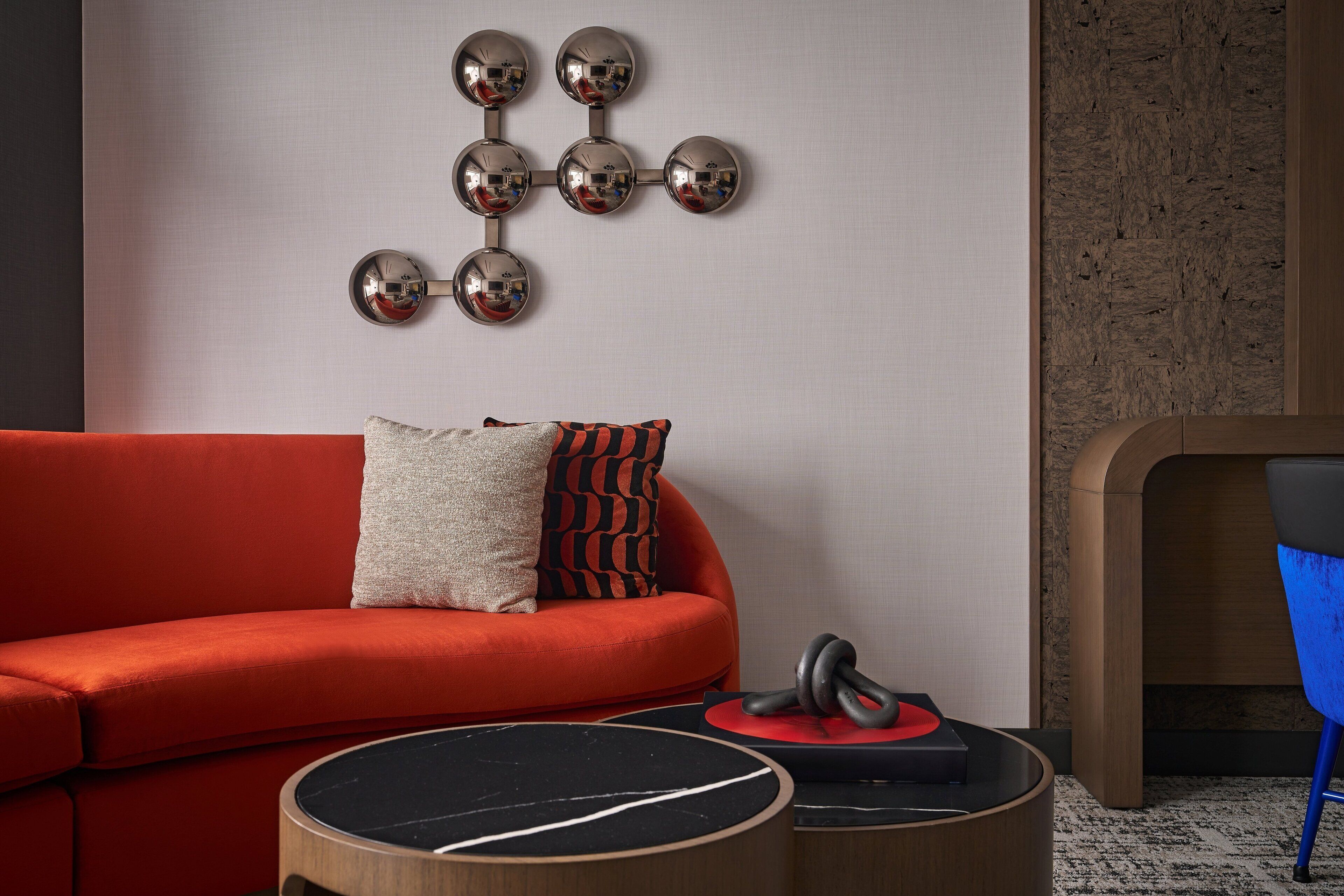 A modern living room with a red sofa, a wall-mounted spherical mirror art piece, a blue chair, and a round wooden coffee table.