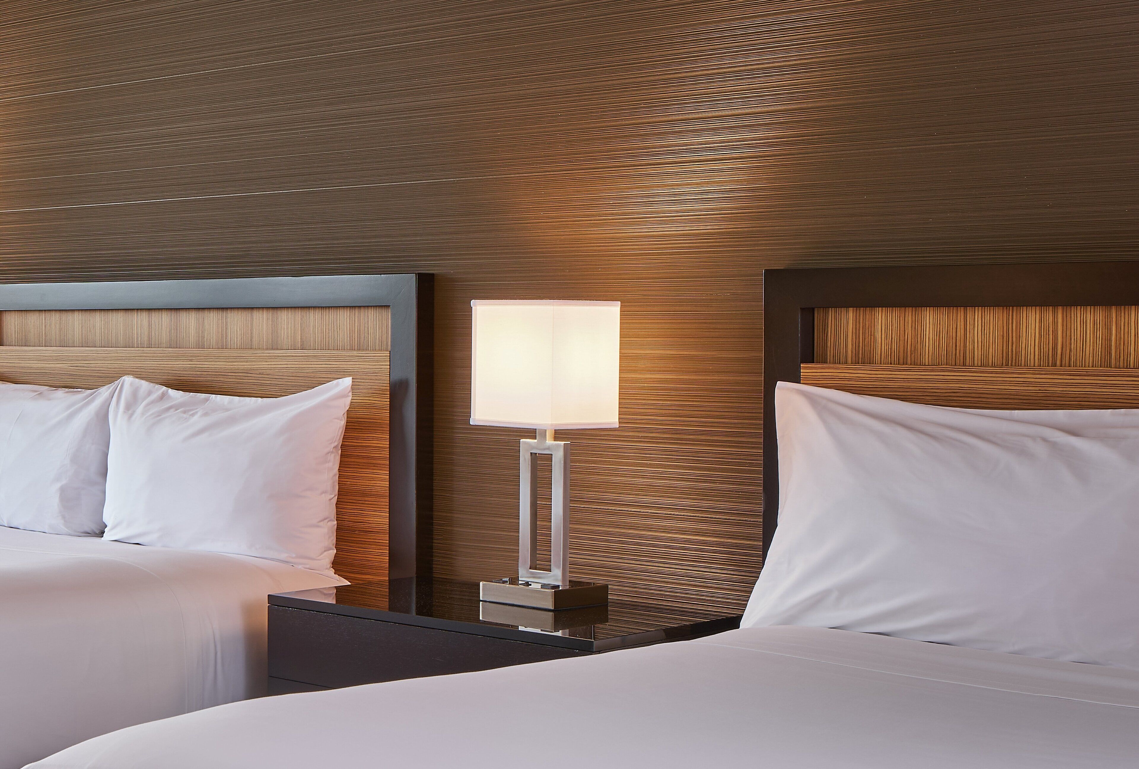 A hotel room with two beds, a nightstand with a lamp, and a wooden headboard.