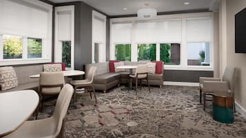 A modern dining area with a large window, a patterned carpet, and a mix of seating options including a bench and chairs.