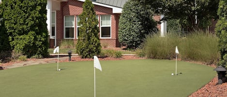 A golf course with three flags, a building with a brick facade, and surrounding greenery.