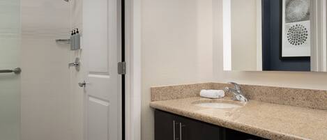 A modern bathroom with a glass shower enclosure, a sink with a granite countertop, and dark cabinetry.