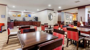 A hotel dining area with multiple tables and chairs, a kitchen in the background, and a mirror on the wall. - Comfort Inn Plover-Stevens Point (Plover)