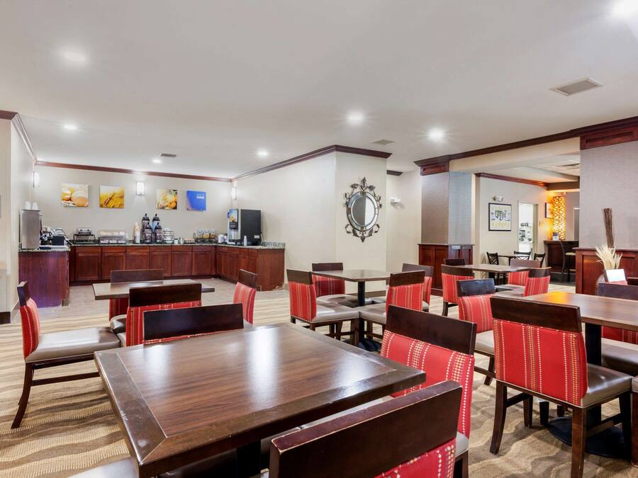 Un comedor de hotel con varias mesas y sillas, una cocina al fondo y un espejo en la pared.