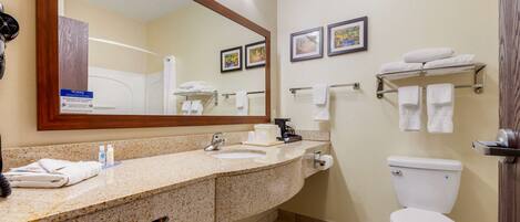 A bathroom with a granite countertop, sink, mirror, toilet, towel rack, and a framed picture on the wall.