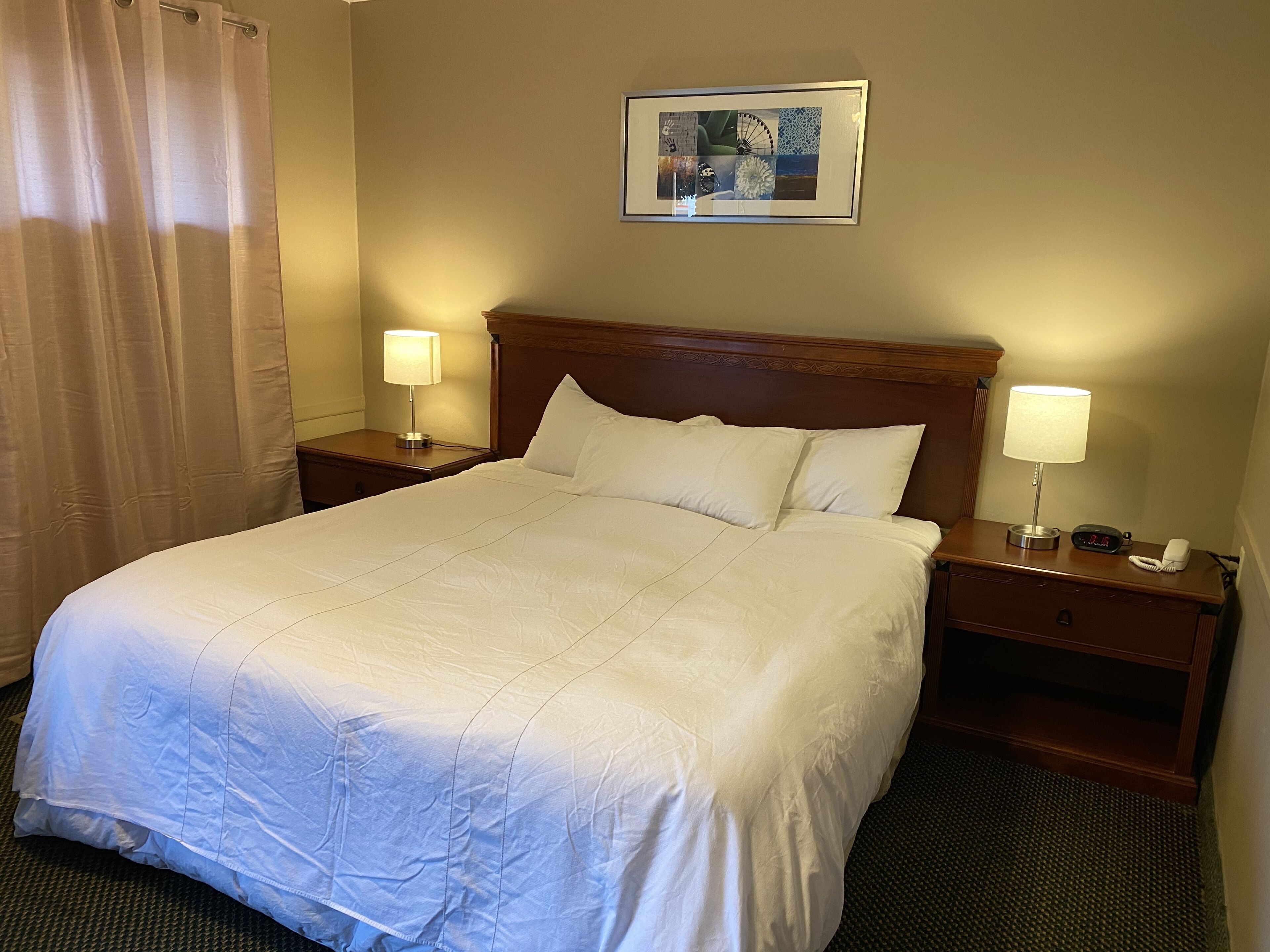 A hotel room with a large bed, two bedside tables with lamps, a framed picture on the wall, and a curtain on the window.