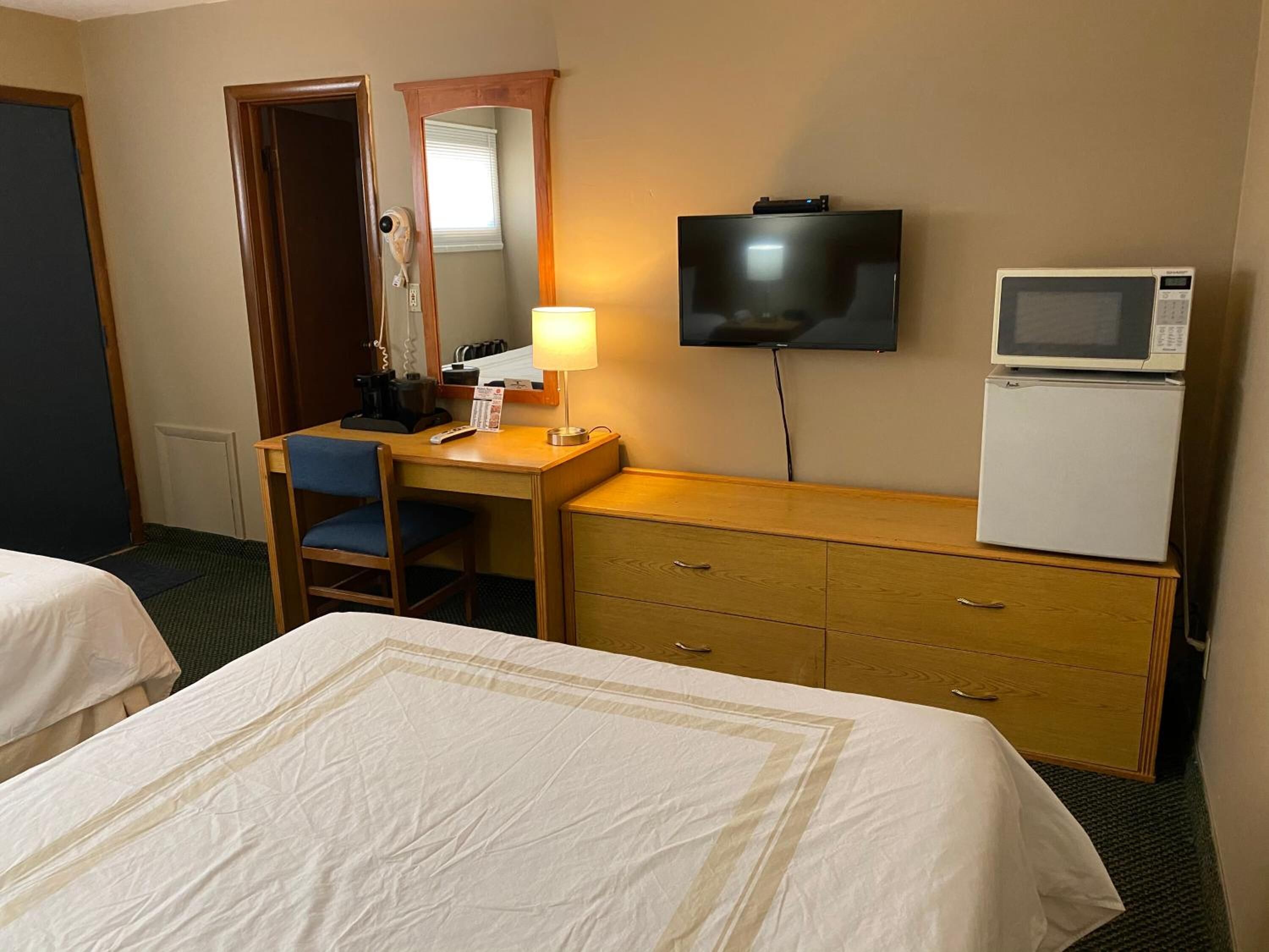 Habitación de hotel con dos camas, un escritorio con silla, televisor, microondas y refrigerador pequeño.