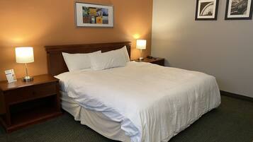 A hotel room with a large bed, two bedside tables with lamps, a nightstand, a framed picture on the wall, and a carpeted floor.