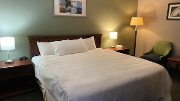 A neatly made bed with white linens, a bedside lamp, a clock, and a framed picture on the wall.