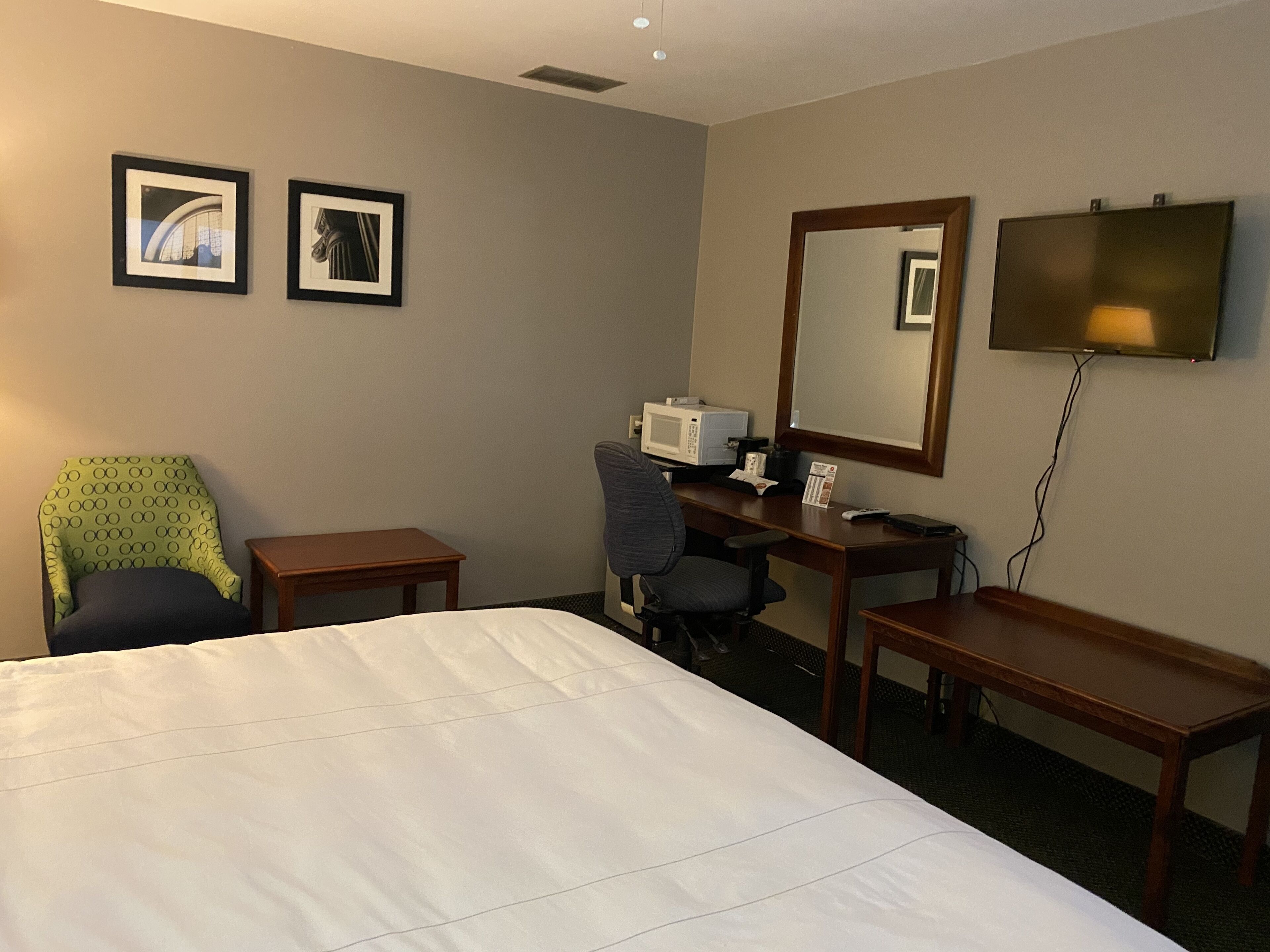 Habitación de hotel con cama, escritorio, silla, televisión y dos cuadros en la pared.