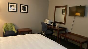 Habitación de hotel con cama, escritorio, silla, televisión y dos cuadros en la pared.