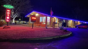 Un motel con letreros de neón, incluyendo un letrero que dice 'Motel' y otro que indica 'No hay habitaciones disponibles', y una bandera estadounidense.
