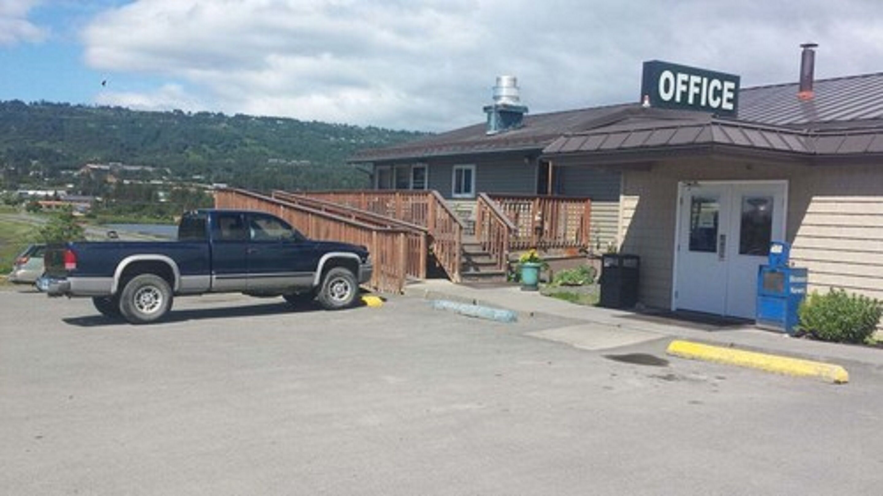 A building with a sign labeled "OFFICE" on the roof, a wooden staircase leading to a door, and a parked truck in front.