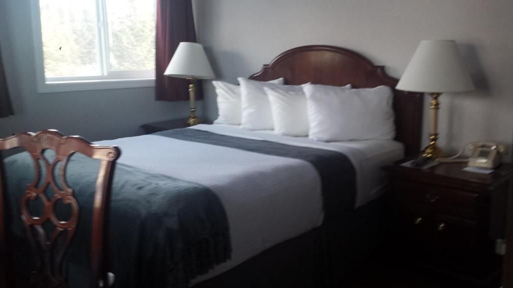 A hotel room with a bed, two bedside lamps, a wooden headboard, a nightstand, and a chair.