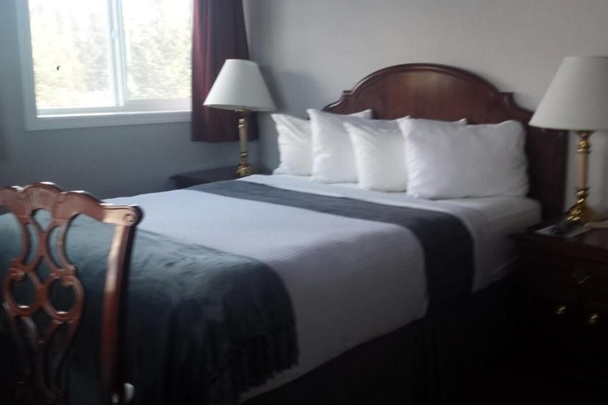 A hotel room with a bed, two bedside lamps, a wooden headboard, a nightstand, and a chair.