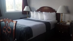A hotel room with a bed, two bedside lamps, a wooden headboard, a nightstand, and a chair. - Beluga Lake Lodge (Homer)