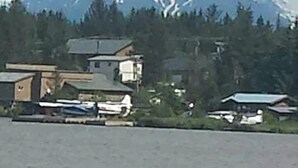 A mountainous landscape with a cabin and a small boat docked near a body of water. - Beluga Lake Lodge (Homer)