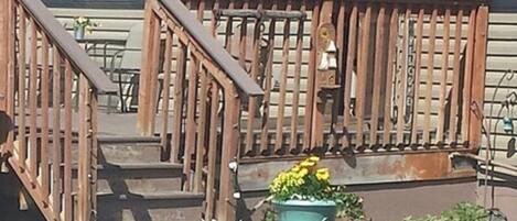 Een woonhuis met een houten trap, een bloempot met gele bloemen en een kleine tuin.